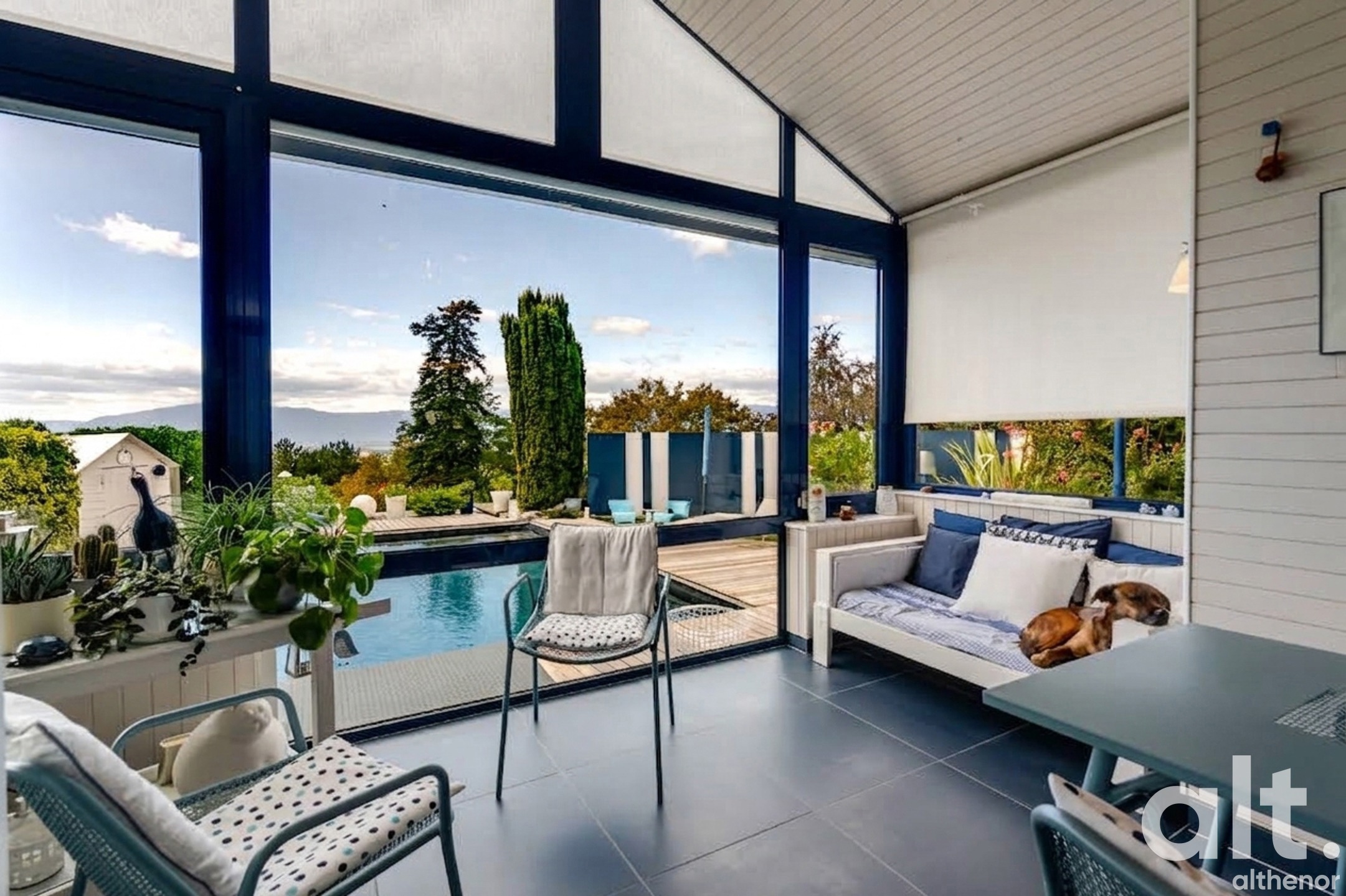 Contemporary interior with French windows opening onto a swimming pool, wooden terrace and mountains in the background, designer furniture and indoor plants.
