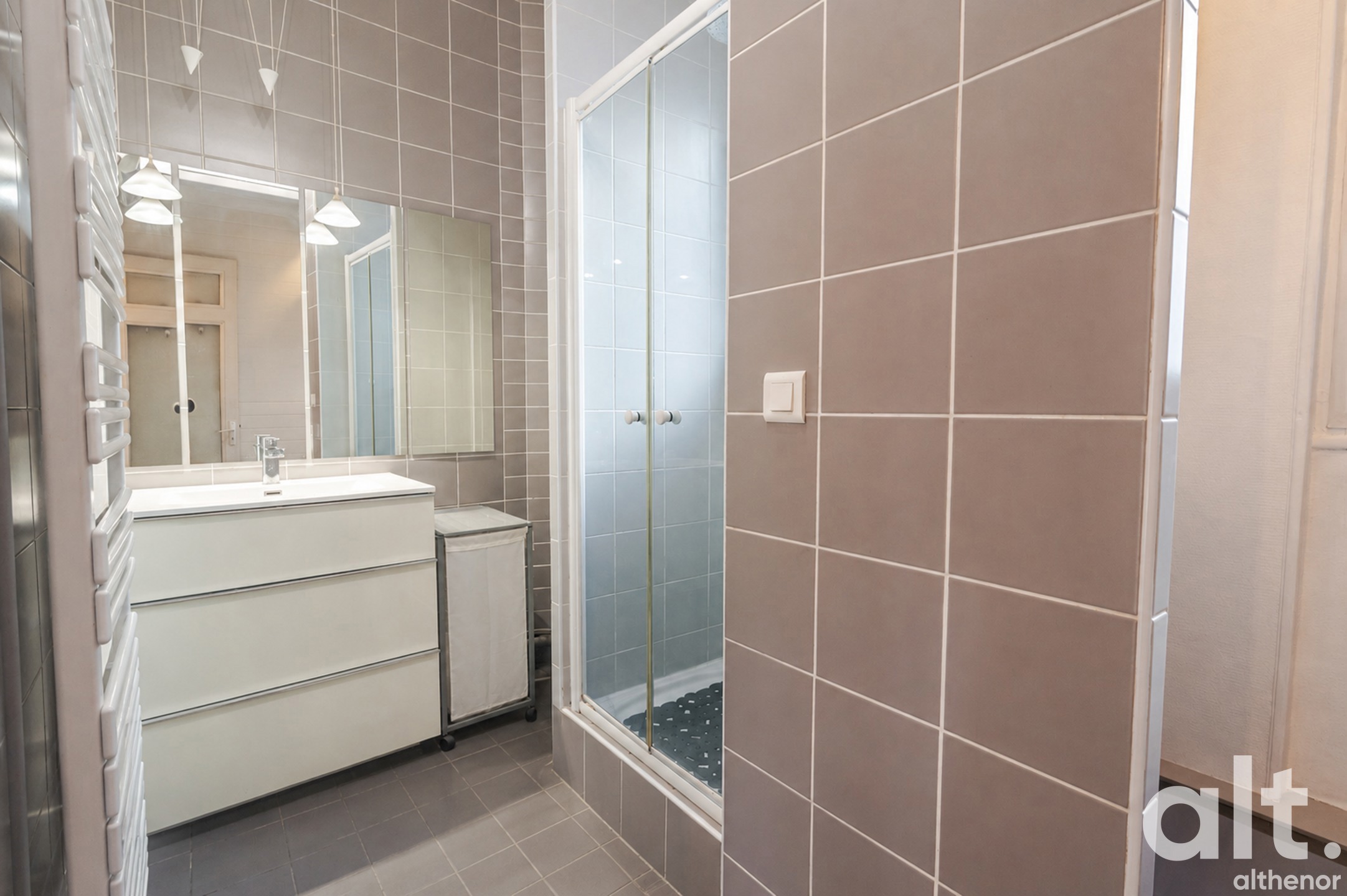 Bathroom with beige and white tiling, white washbasin with illuminated mirror, glassed-in walk-in shower and heated towel rail.